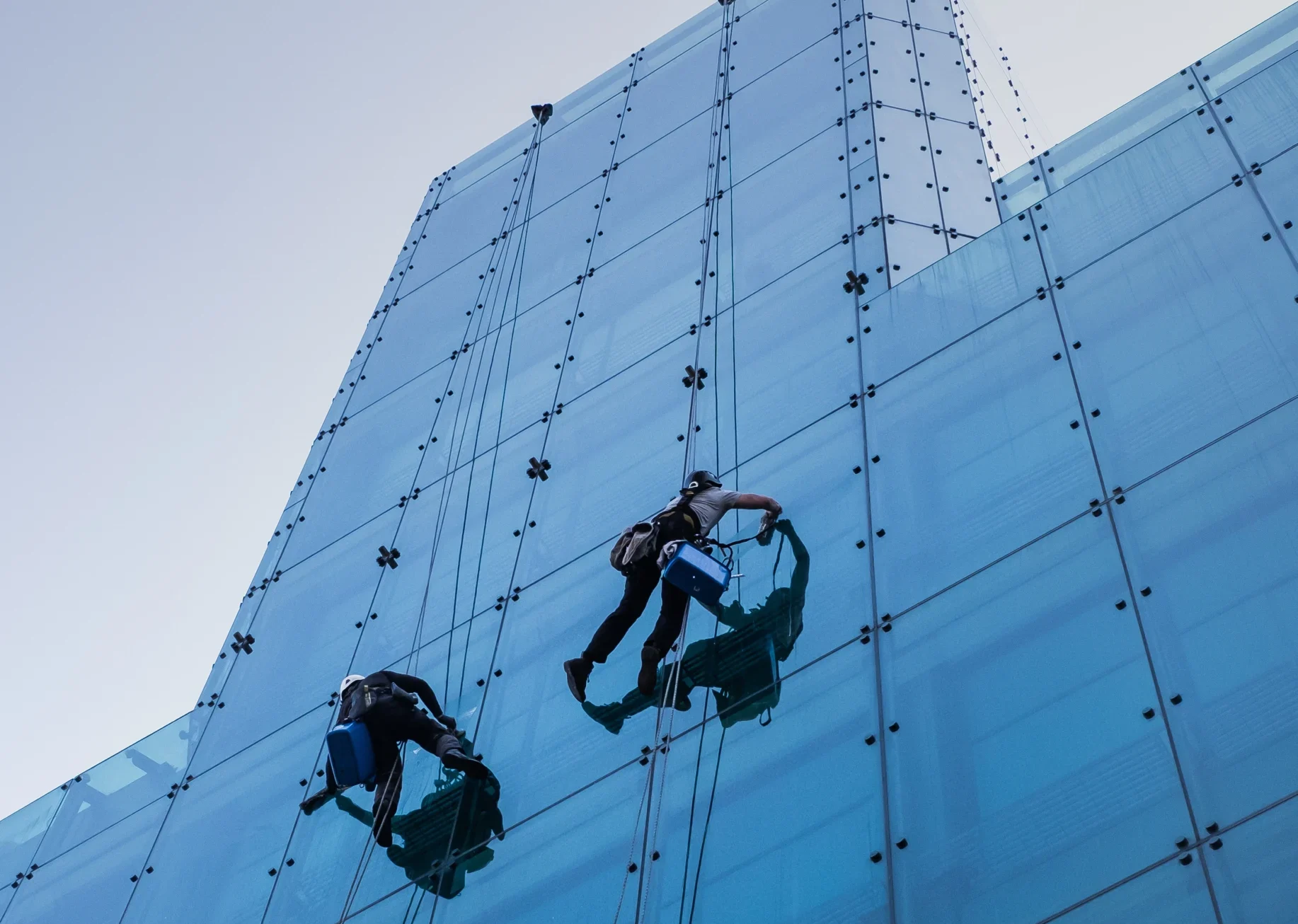 vertical-low-angle-shot-two-people-climbing-tall-glass-building-day-time